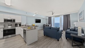 Une cuisine moderne équipée d’appareils électroménagers en acier inoxydable, un coin repas avec une table et des chaises, un salon avec un canapé et un balcon offrant une vue agréable.