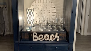 Ein dunkelblauer Schrank mit Zierelementen oben, ein Schild mit der Aufschrift „Beach“ sowie Weingläser und ein Kerzenhalter.