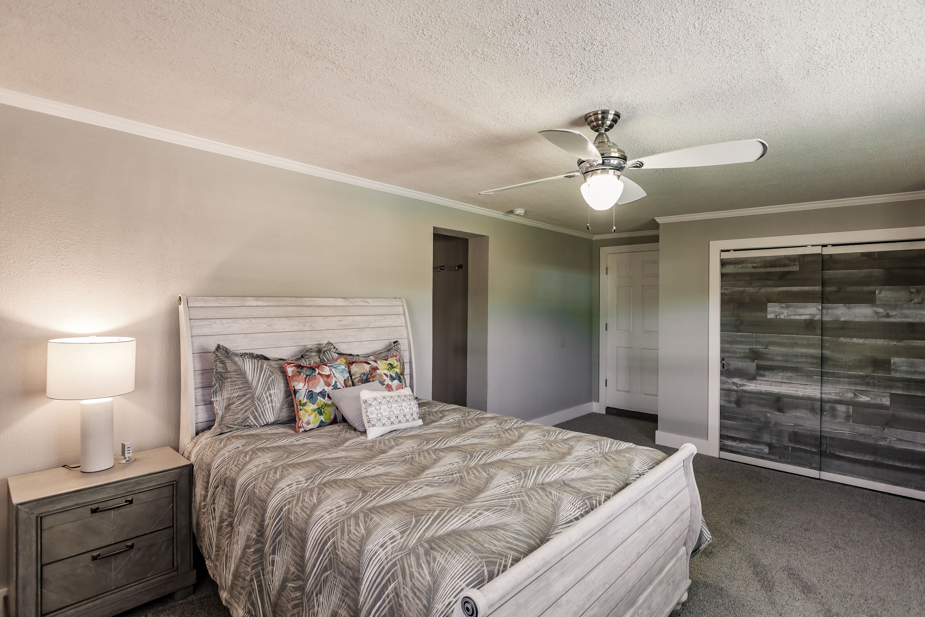 Une chambre à coucher comprenant un lit, une table de chevet, une lampe, un ventilateur de plafond et une armoire.