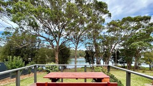 Un banc en bois sur une terrasse donnant sur une rivière, avec des arbres et une clôture en arrière-plan.