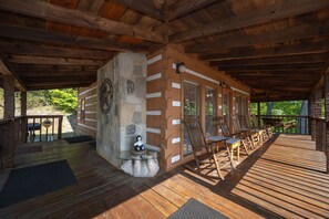 A covered wooden deck with a stone pillar, wooden chairs, and a table. - Cabin of Dreams Beautiful Mountain Views • Hot Tub • Near Dollywood & Gatlinburg (Pigeon Forge)
