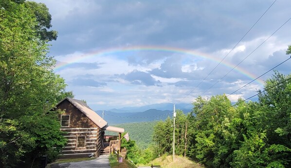 A wooden cabin with a porch, surrounded by lush greenery and mountains in the background. - Cabin of Dreams Beautiful Mountain Views • Hot Tub • Near Dollywood & Gatlinburg (Pigeon Forge)