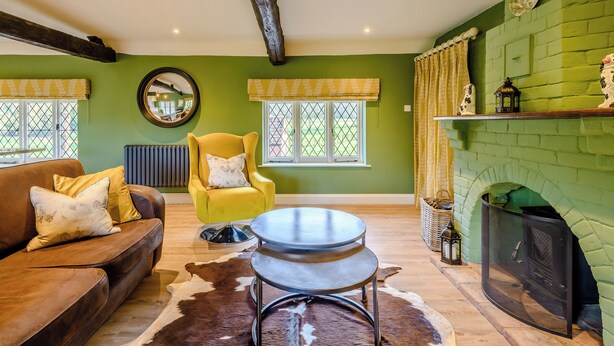 A living room with a brown leather sofa, a yellow armchair, a round metal table, and a green brick fireplace.