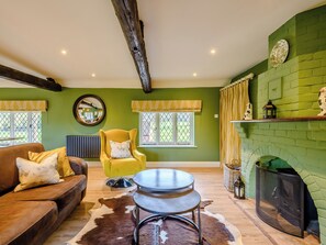 A living room with a brown leather sofa, a yellow armchair, a round metal table, and a green brick fireplace.