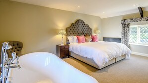 A bedroom with a large bed, two bedside lamps, a radiator, and a window with curtains.