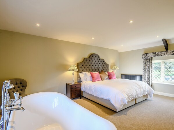 A bedroom with a large bed, two bedside lamps, a radiator, and a window with curtains.