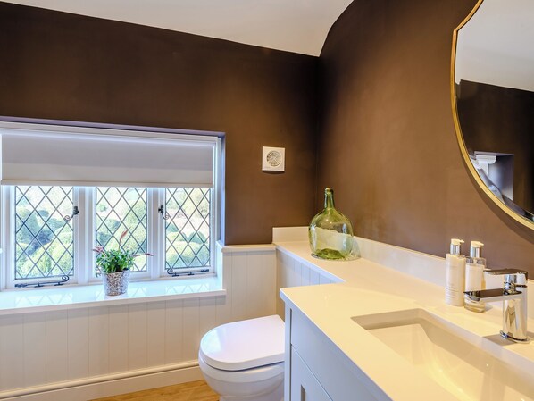 A bathroom with a white vanity, a large mirror, a window with a view of greenery, and a white toilet.
