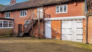 A brick building with a tiled roof, a wooden staircase leading to a landing, and a white garage door.