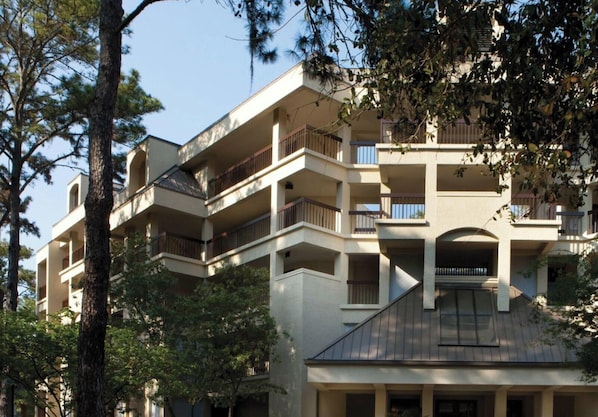 Un edificio a più piani con balconi, un tetto piatto e un albero sullo sfondo.