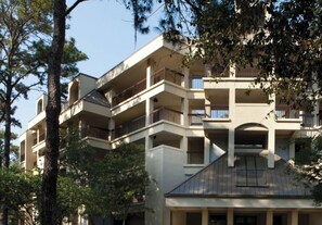 A multi-story building with balconies, a flat roof, and a tree in the foreground.