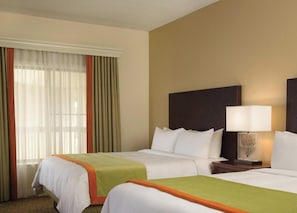 A hotel room with two beds, a nightstand with a lamp, and a window with curtains.