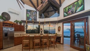 A modern kitchen with a bar area, large windows, and a view of the ocean. - Villa Costa Mar Ocean View Guard Gated Community (Playa Hermosa, Carrillo)