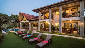 A modern two-story house with a well-maintained lawn, outdoor seating area with lounge chairs, and a pool. - Villa Costa Mar Ocean View Guard Gated Community (Playa Hermosa, Carrillo)