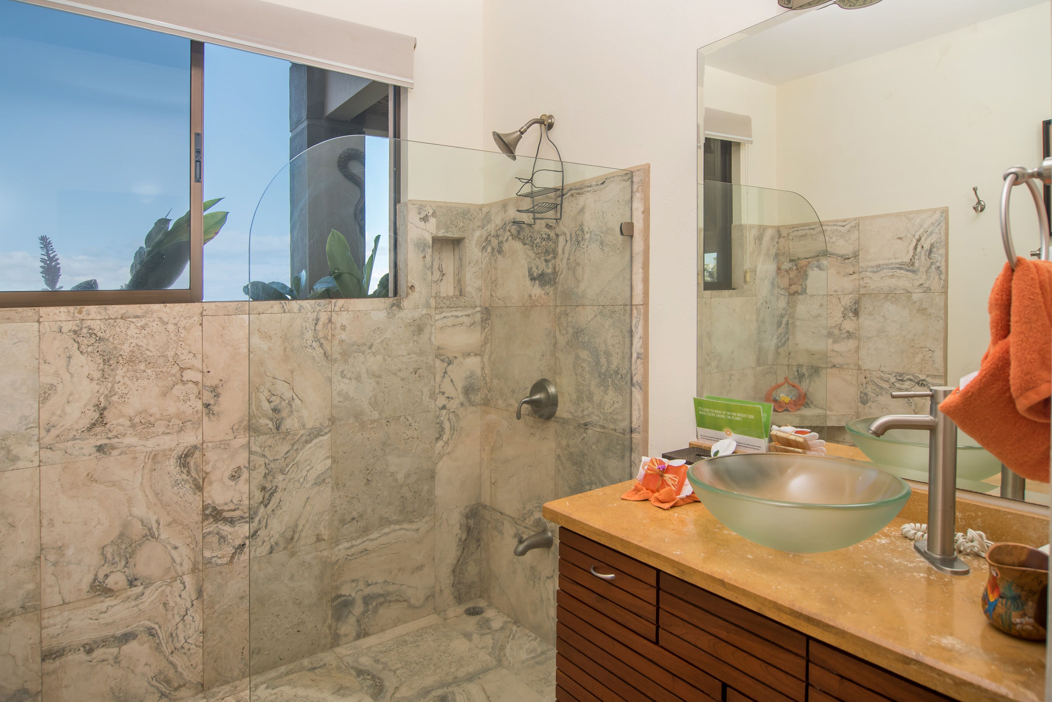 A bathroom with a glass shower enclosure, a large mirror, a marble-tiled wall, and a wooden vanity.