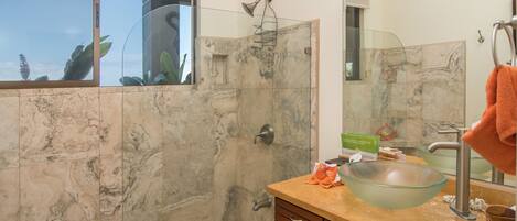 A bathroom with a glass shower enclosure, a large mirror, a marble-tiled wall, and a wooden vanity.