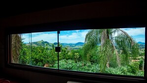 Ein Zimmer mit einem großen Fenster, das einen Blick auf eine üppige Landschaft mit Hügeln und viel Grün bietet.