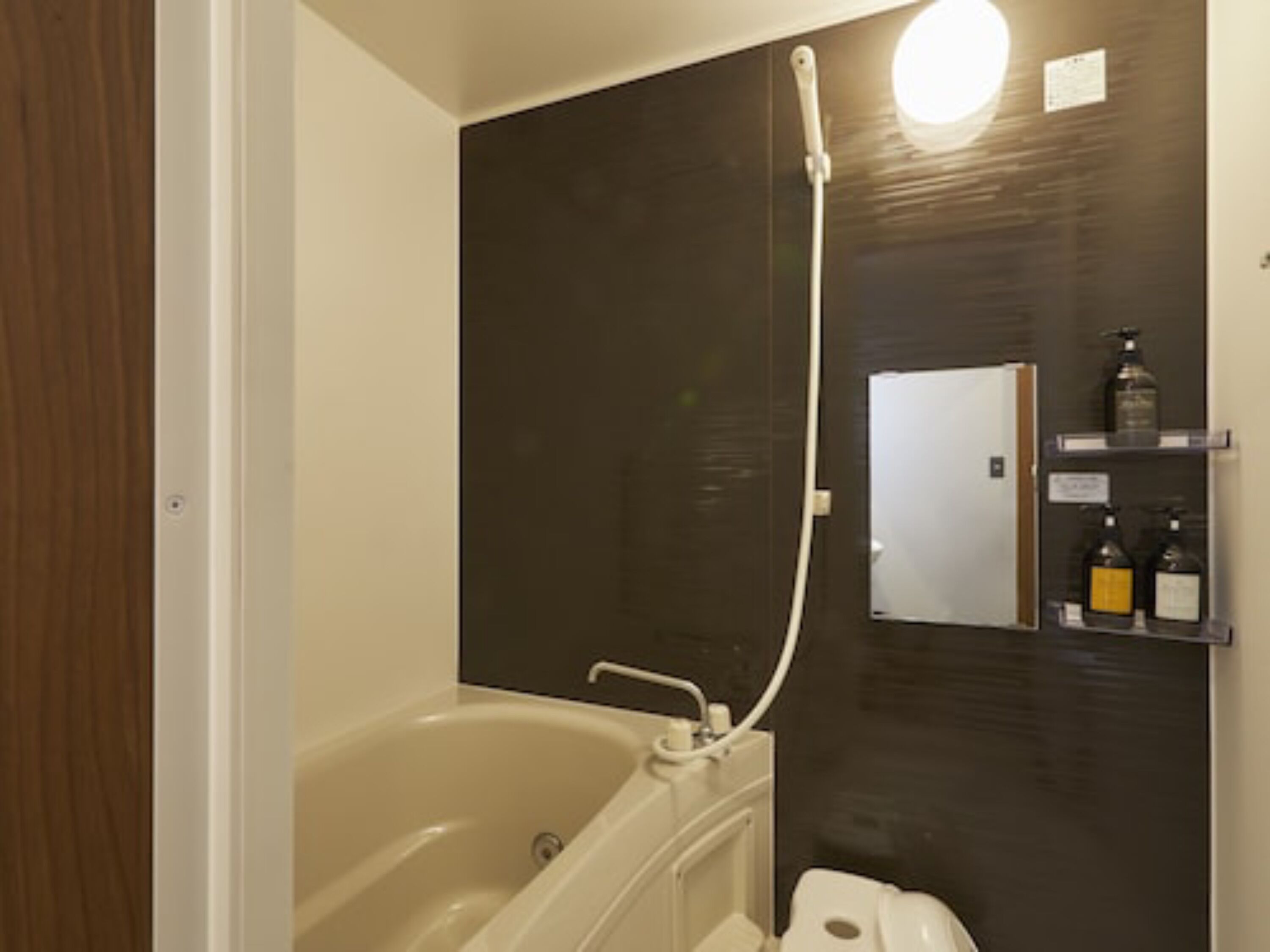 Un bagno con vasca, doccia e specchio. Sono presenti articoli da toilette su uno scaffale.