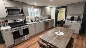 A modern kitchen with stainless steel appliances, a wooden dining table, and light-colored cabinetry.