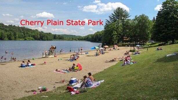 Cherry Plain State Park with a sandy beach, people relaxing, and a lake.