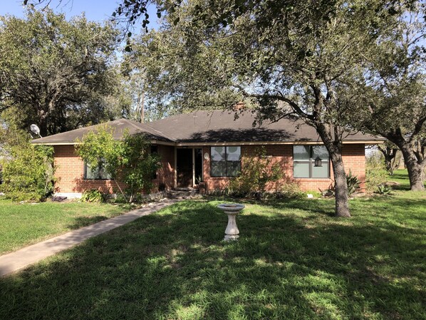 A single-story brick house with a front porch, a satellite dish, and a well-maintained lawn. - Four bedroom country home. (Kingsville)