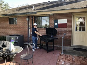 A brick building with a flag, a grill, a table with chairs, and a window. - Four bedroom country home. (Kingsville)