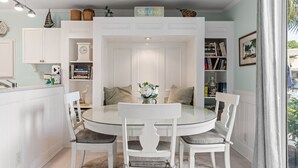 A dining area with a round table and white chairs, surrounded by white cabinetry and shelves with books and decorative items.