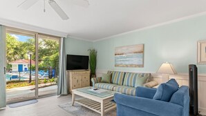 A living room with a blue sofa, a striped couch, a flat-screen TV, and a view of a pool through a sliding glass door.