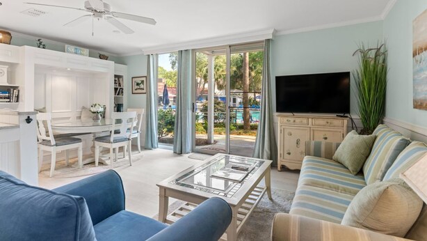 A spacious living room with a large TV, a ceiling fan, and a view of a pool through the glass doors.