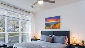 Un dormitorio moderno con una cama grande, un ventilador de techo y vistas al exterior a través de amplios ventanales.