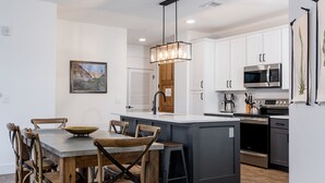 Una cocina moderna con armarios blancos, una isla central y un comedor con sillas de madera.