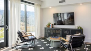 Una sala de estar moderna con un televisor grande, dos sillones, una mesa de centro redonda y vistas al exterior a través de un puerta corrediza.