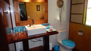 Ein Badezimmer mit einem Holzkosmetikschrank, einem weißen Waschbecken, einer blauen Toilette und einem Spiegel über dem Waschbecken.
