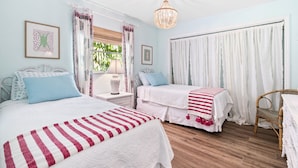 A bedroom with two beds, a chandelier, a wicker chair, and a window with curtains. - Tequesta/Jupiter Pool Home close to Beaches and Dining. 2 miles to the beach. (Tequesta)
