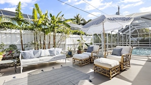 A covered outdoor seating area with a white fence, potted plants, and a pool. - Tequesta/Jupiter Pool Home close to Beaches and Dining. 2 miles to the beach. (Tequesta)