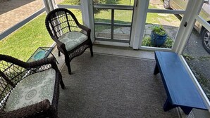 Eine überdachte Veranda mit Korbstühlen und einer Bank, eine amerikanische Flagge und Blick auf die Straße.