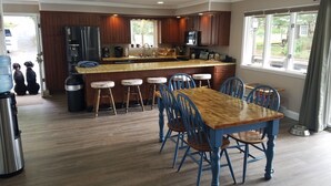 A modern kitchen with wooden cabinets, a central island, bar stools, and a dining table with blue chairs. - Chalet Ripple-Lake Harmony- Lakefront- 5 Bedroom 3.5 bath- near Restaurants/Bars (Lake Harmony)