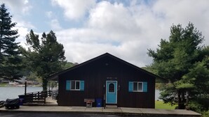 A small cabin with a blue door and windows, located near a body of water with trees around. - Chalet Ripple-Lake Harmony- Lakefront- 5 Bedroom 3.5 bath- near Restaurants/Bars (Lake Harmony)