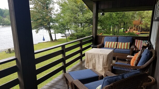 A covered outdoor seating area with wicker furniture and a view of a lake. - Chalet Ripple-Lake Harmony- Lakefront- 5 Bedroom 3.5 bath- near Restaurants/Bars (Lake Harmony)
