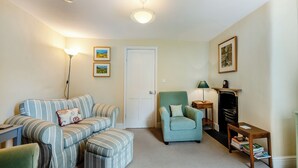 A living room with a striped sofa set, a teal armchair, a small side table with a lamp, and a bookshelf.