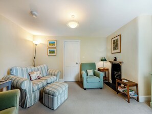 Un salon comprenant un canapé à rayures, un fauteuil turquoise, une petite table d’appoint avec une lampe et une bibliothèque.