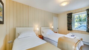 A room with two beds, a window with curtains, a door, and a wall-mounted light fixture.