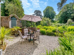 A patio with a table and chairs, surrounded by a gravel path and lush greenery.