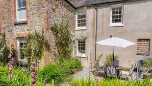 A stone building with a garden patio featuring outdoor seating and a white umbrella.