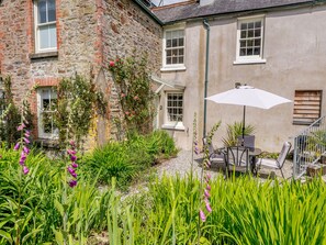 Un bâtiment en pierre doté d’un patio avec jardin, comprenant un espace salon extérieur et un parasol blanc.
