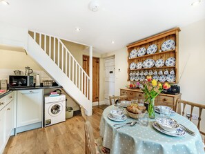 A kitchen with a microwave, washing machine, and a dining area with a table set for two.