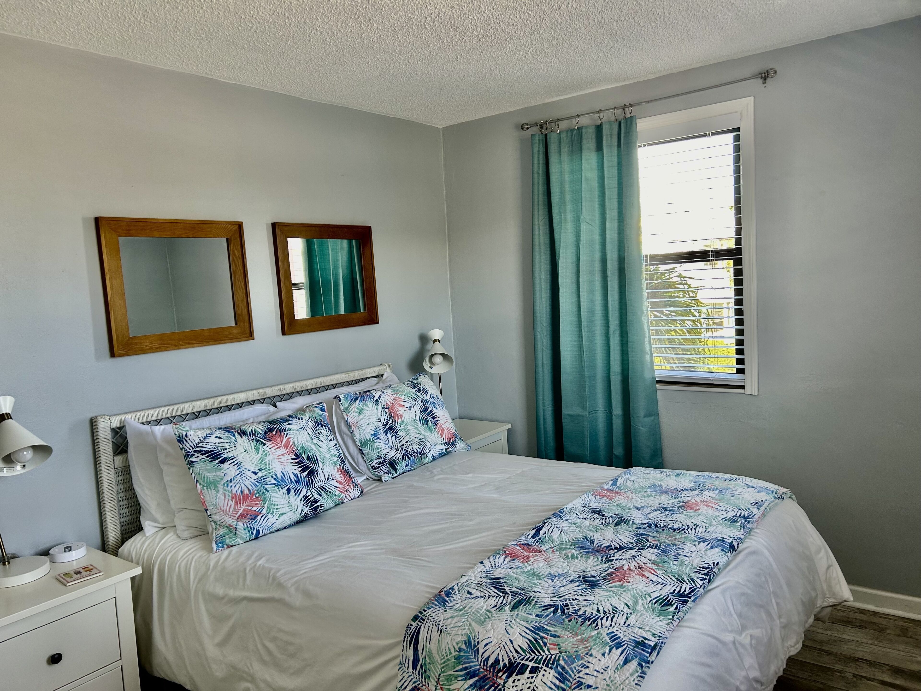 A bedroom with a bed, two mirrors, a bedside table with a lamp, and a window with curtains.