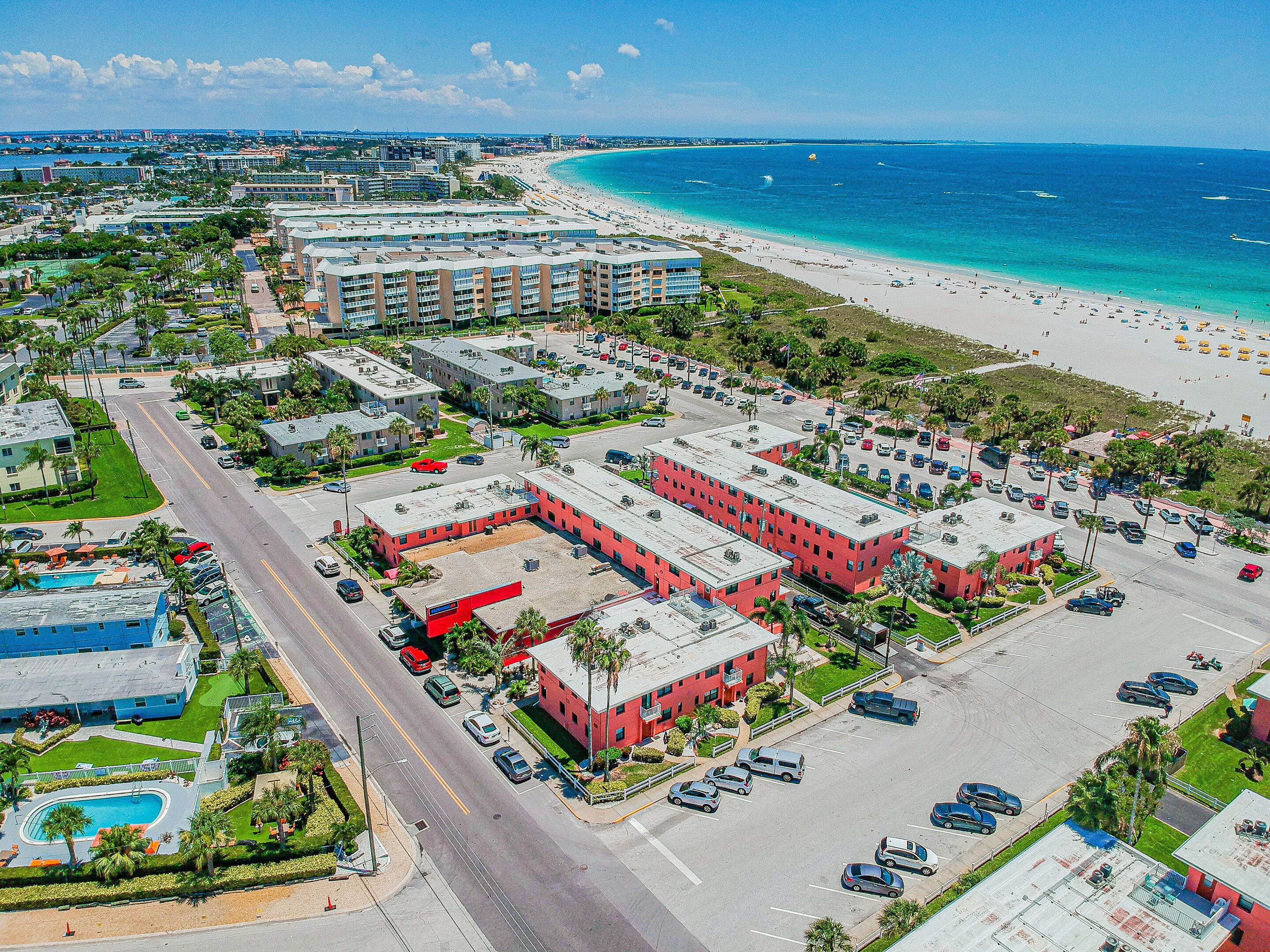 Un hotel costero con varias edificaciones, un estacionamiento y una playa al fondo.