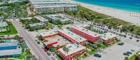 Un hotel costero con varias edificaciones, un estacionamiento y una playa al fondo.