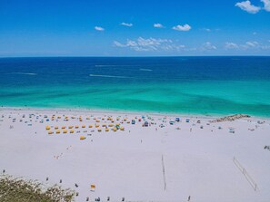 A beach with numerous umbrellas and sun loungers, a clear blue sky, and calm ocean waters.