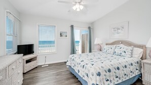 A bedroom with a bed, a television, a ceiling fan, and a view of the sea through the window. - Oceanfront stunner in Emerald Isle (Emerald Isle)